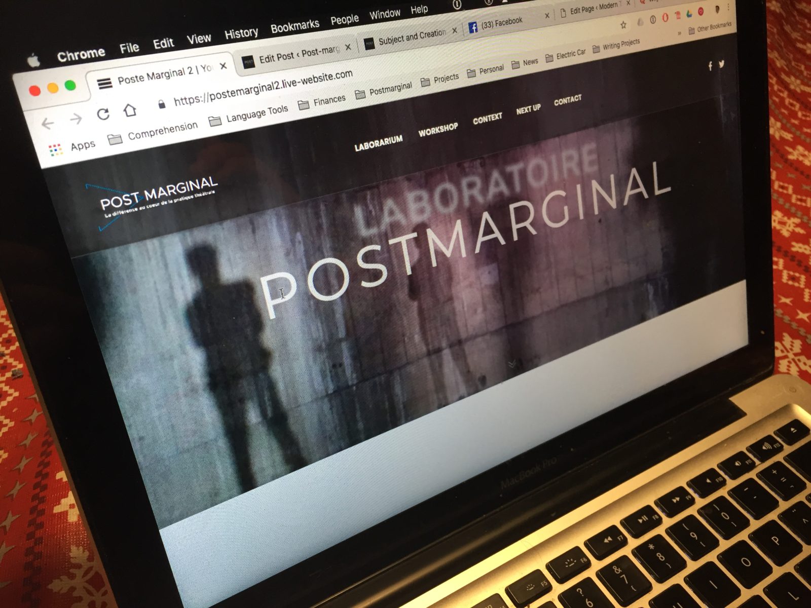 Un écran d’ordinateur portable affiche le nouveau site Laboratoire Postmarginal, avec l’ombre d’une silhouette sur un mur texturé.