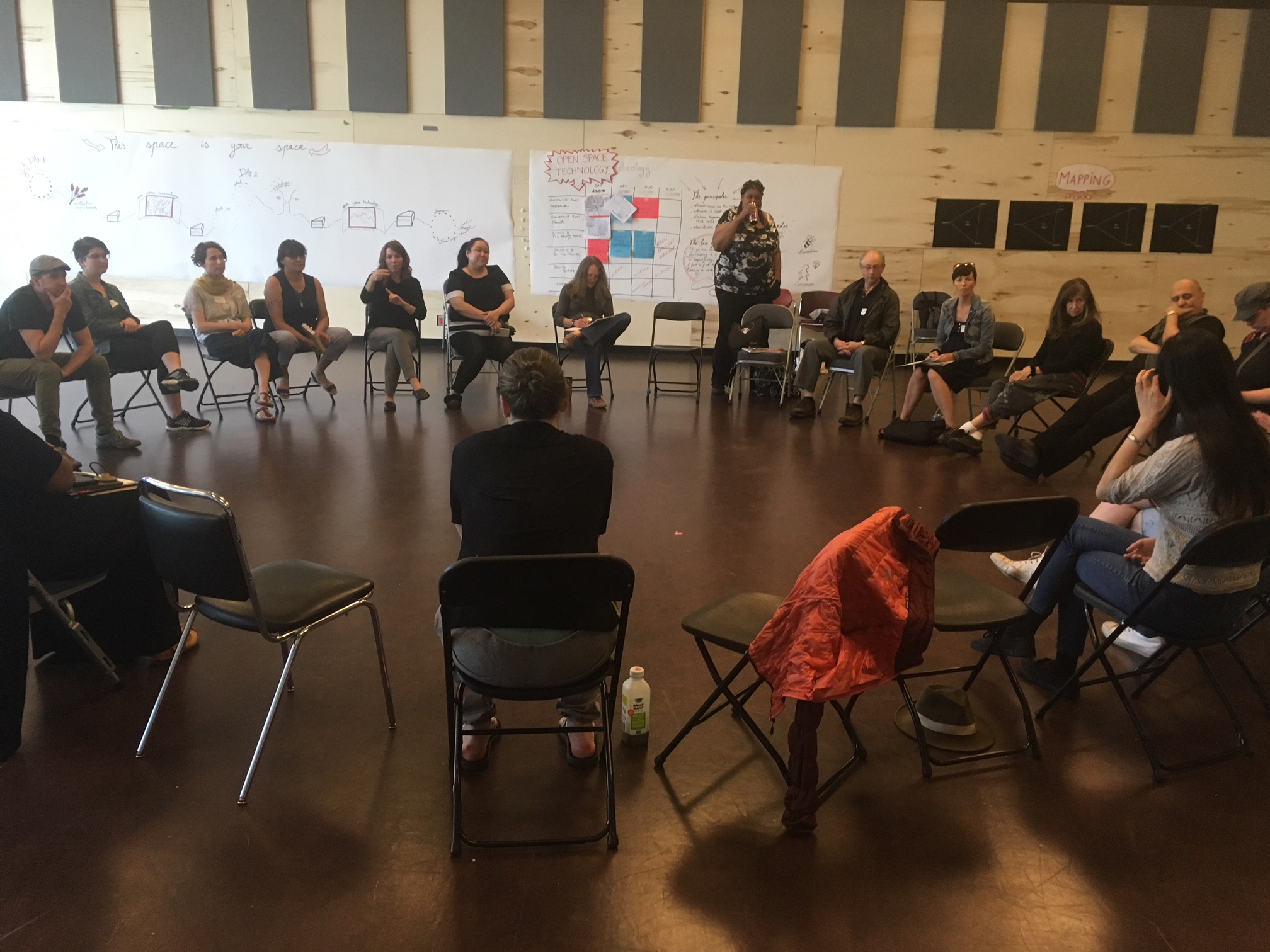Participants in a large circle of chairs in a wood-panelled studio during the 2019 Laborarium in Vancouver.
