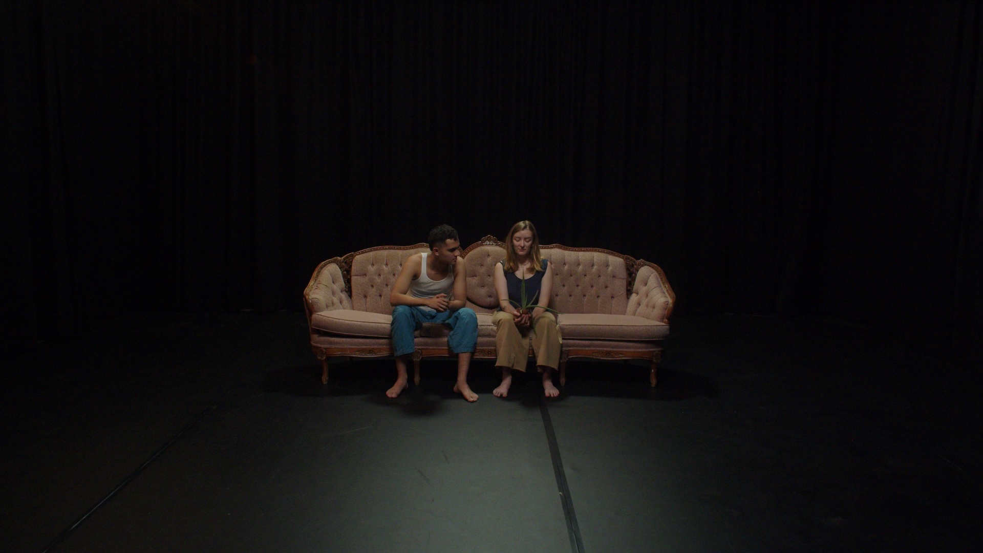 A man and a woman sit apart from each other on a salmon pink couch
