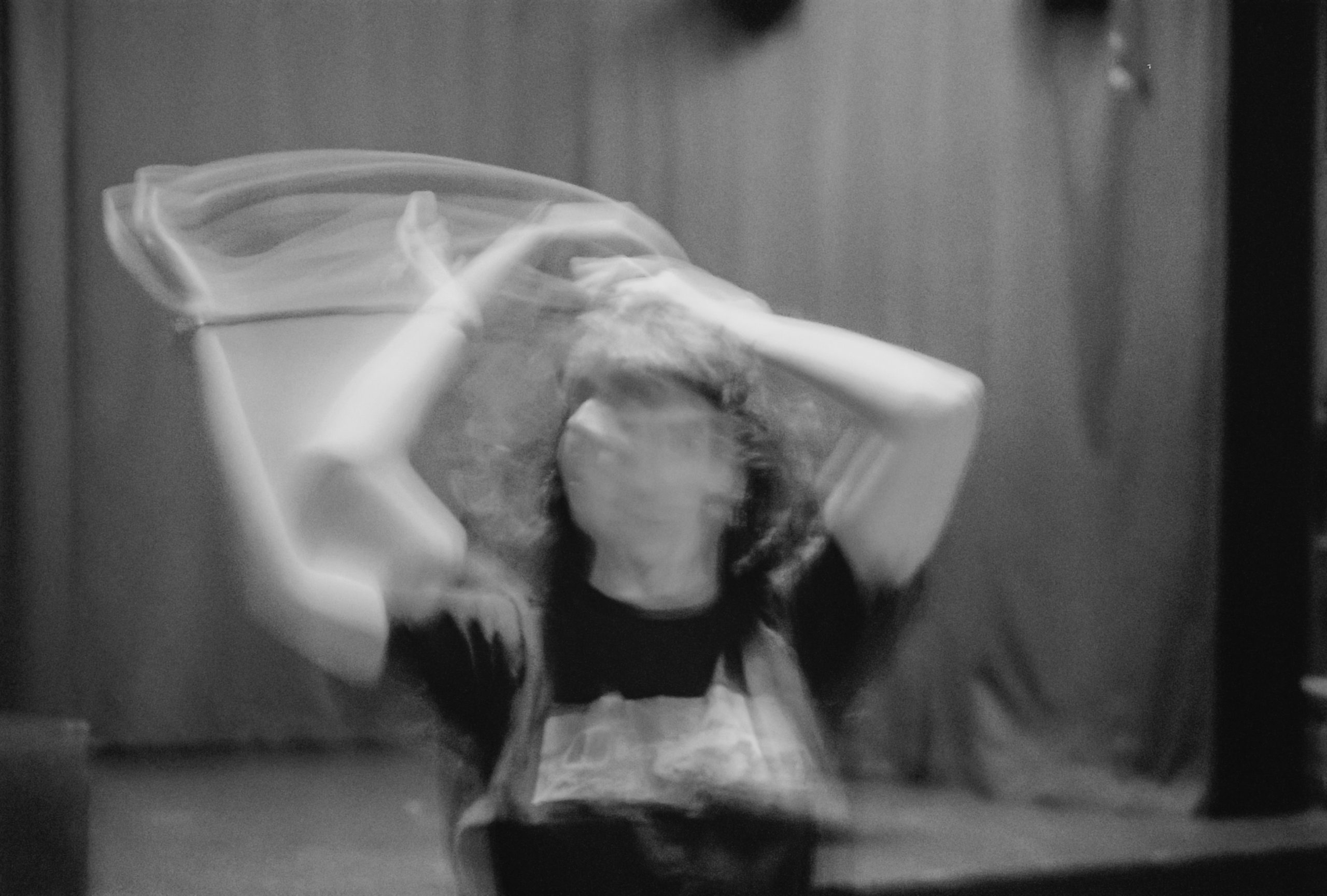 Black-and-white photo of a performer spinning on stage, arms raised and blurred with motion.