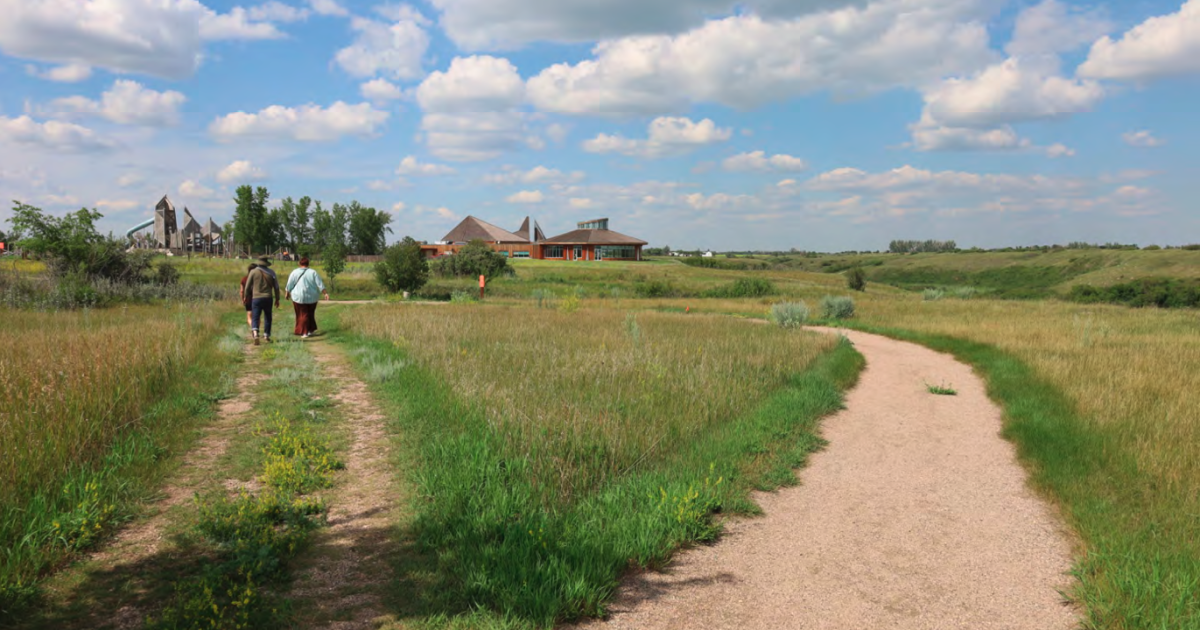 Three people walk away from the camera down a country road that has forked into two.