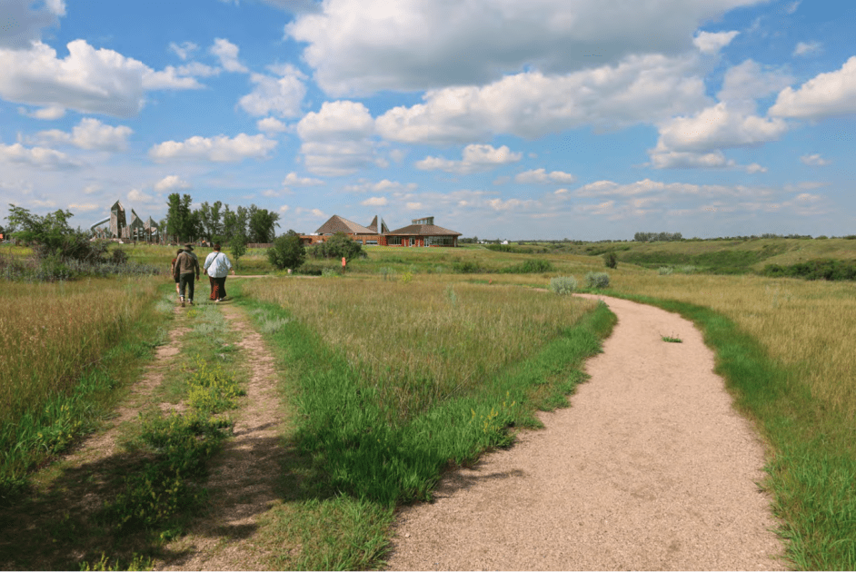 Three people walk away from the camera down a country road that has forked into two.