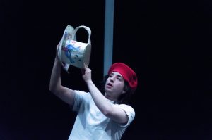 A man in a red hat holds up an oversized teacup and saucer.